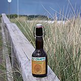 Bierflasche auf dem Holzgeländer an einer mit Strandgras bewachsener Düne